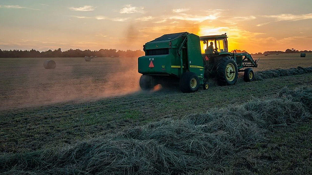Hay harvester in field with sun setting in the background